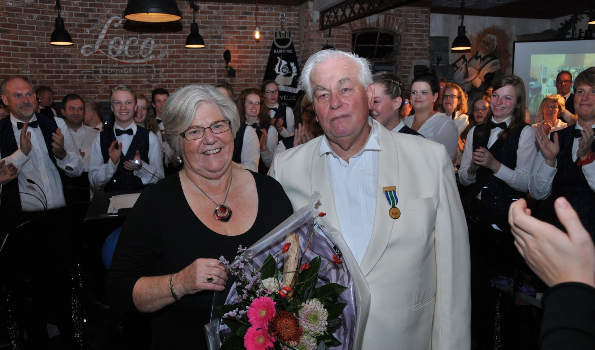 Willem en Trijntje Loff voor het orkest. Willem Loff draagt hierbij de aan hem uitgereikte medaille van verdienste van het CSIM. Foto: PR