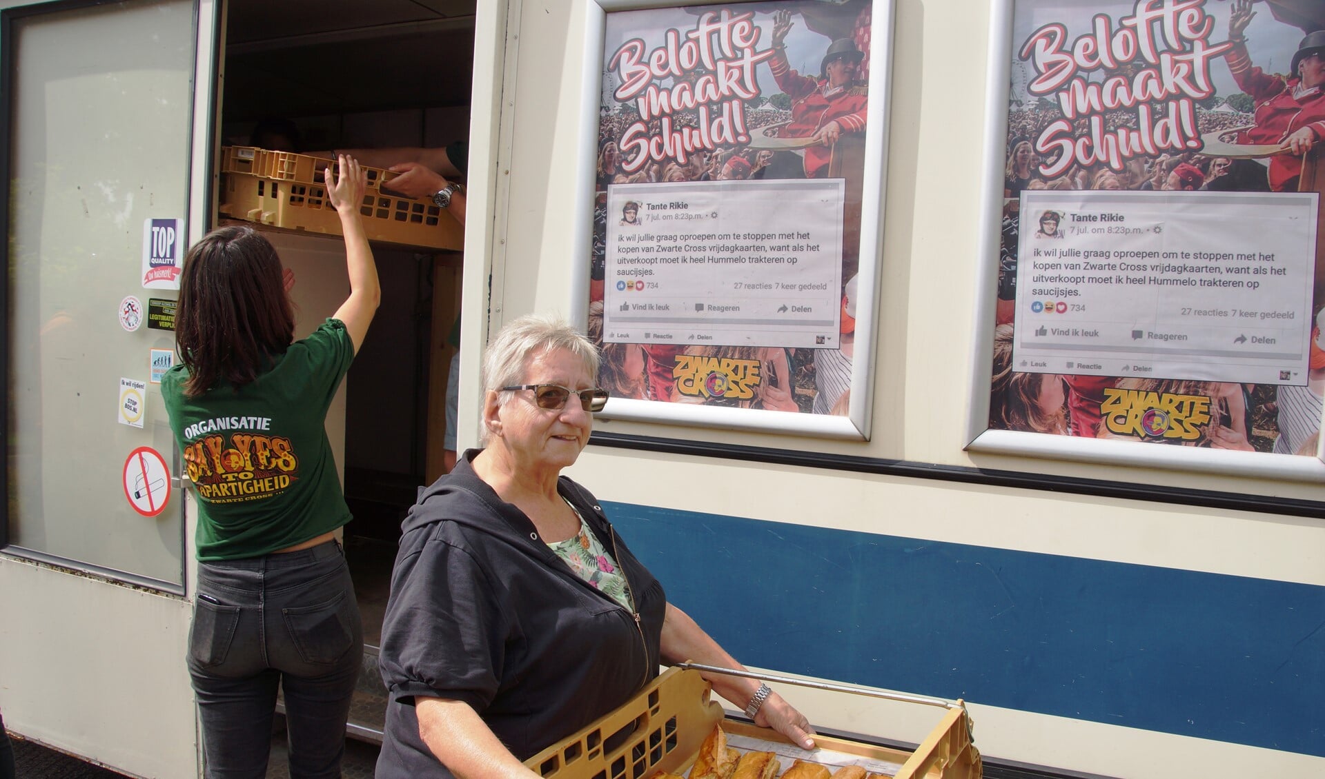 Tante Rikie stapt uit de SRV-wagen met een bak saucijzenbroodjes. Op de achtergrond de tweet waarin ze belooft Hummelo te trakteren. Foto: Gerwin Nijkamp