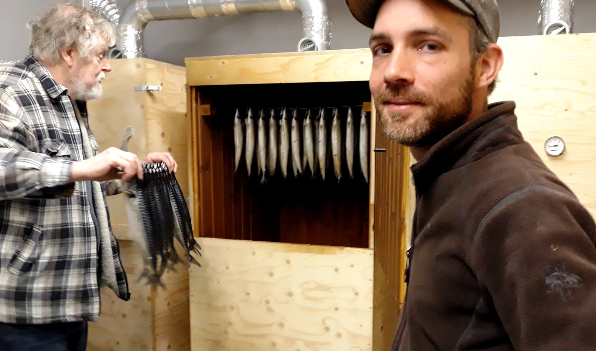 Hans hangt een speet paling in de houten rookkast. Björn houdt de deur open. Foto: Meike Wesselink