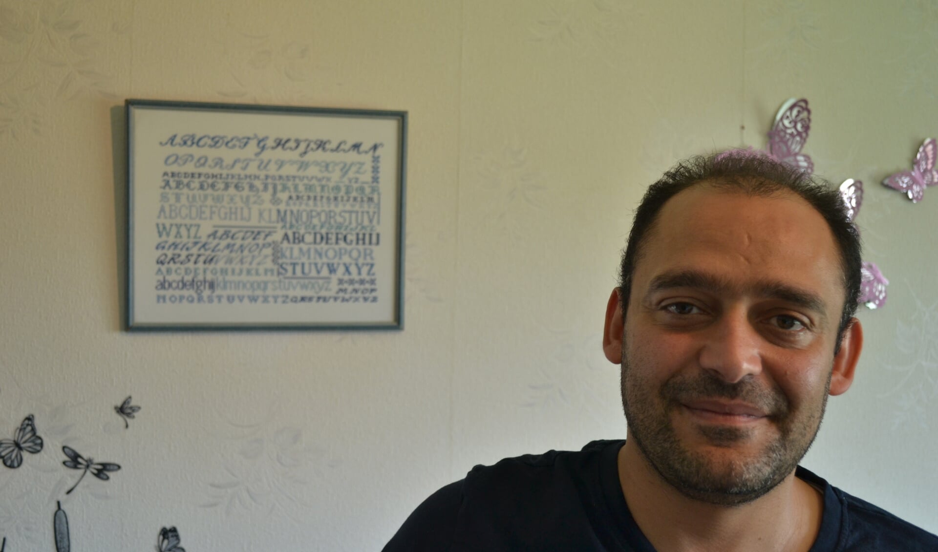 Ghasoub in zijn woonkamer bij het Nederlandse alfabet, geborduurd door zijn taaldocente Truus Bulten. Foto Leander Grooten 