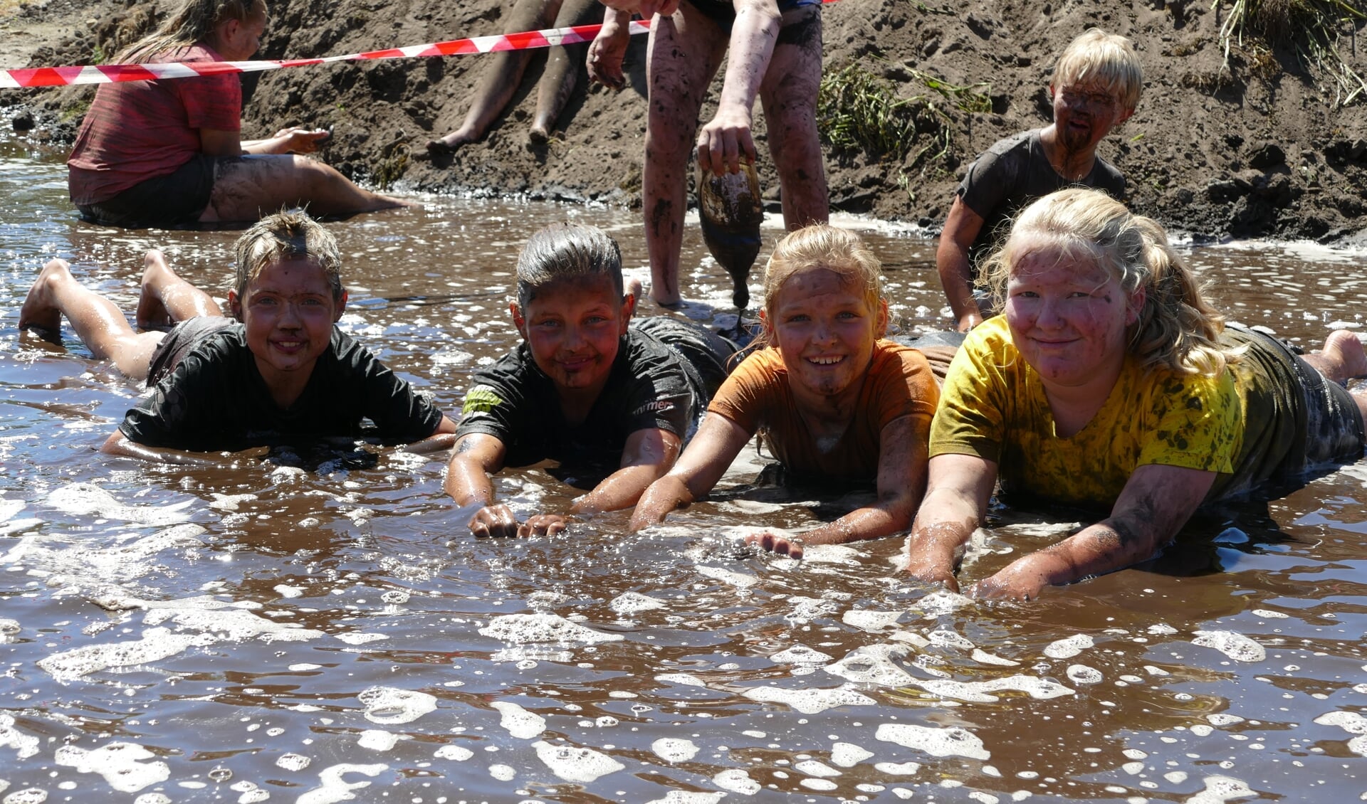 Met grote en kleine zwembanden beklommen de kinderen de steile berg zwarte grond om er uiteindelijk met een snelheid af te roetsjen op de met groene zeep ingesmeerde baan. Foto: PR. 