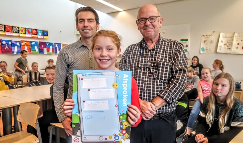 Basisschoolleerlinge Kimberley Korten (11) en wethouder Paul Hofman (links) zetten maandagmiddag hun handtekening tegen het gebruik van een mobieltje op de fiets. Rechts gastdocent Rob Roor van Veilig Verkeer Nederland. Foto Luuk Stam