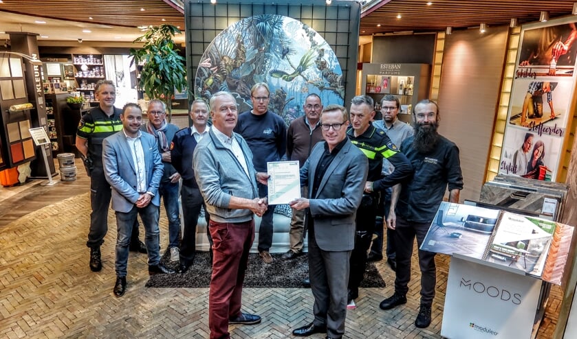 Ondernemer Bennie Harmsen (vooraan, links) krijgt het certificaat dat hoort bij het Keurmerk Veilig Ondernemen uitgereikt door wethouder Willem Buunk. Achter hen ondernemers uit de gemeente Bronckhorst en leden van de politie en de brandweer. Foto: Luuk Stam