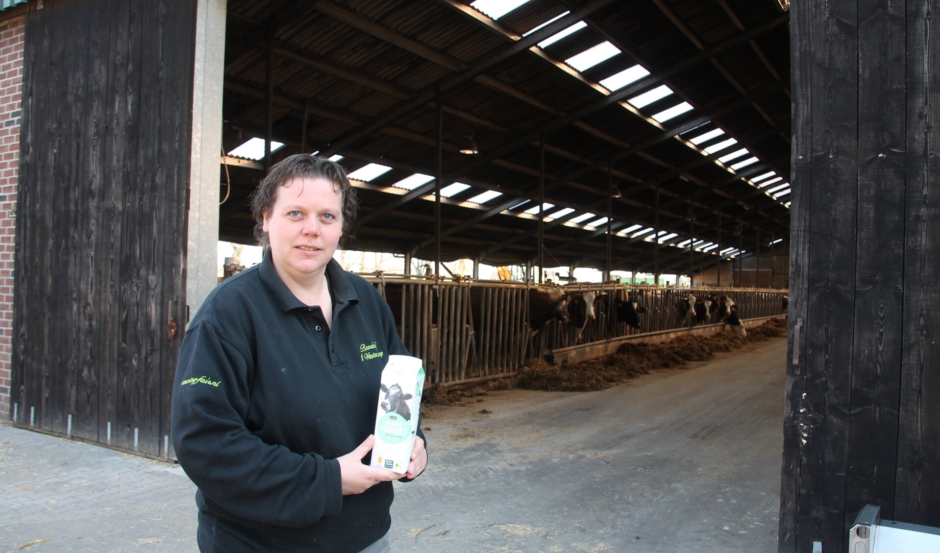 Suzanne Ruesink met een pak Beter Leven-zuivel, voor de stal met de 'leveranciers' van de melk. Foto: Lydia ter Welle