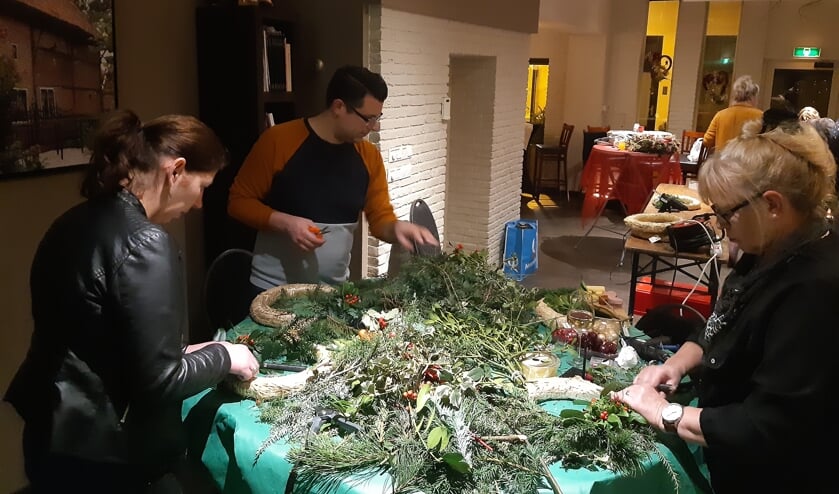 Uit een tafel vol groen zoeken enkele deelnemers naar passende takken voor hun kerstkrans. Foto: PR Goed Geaard