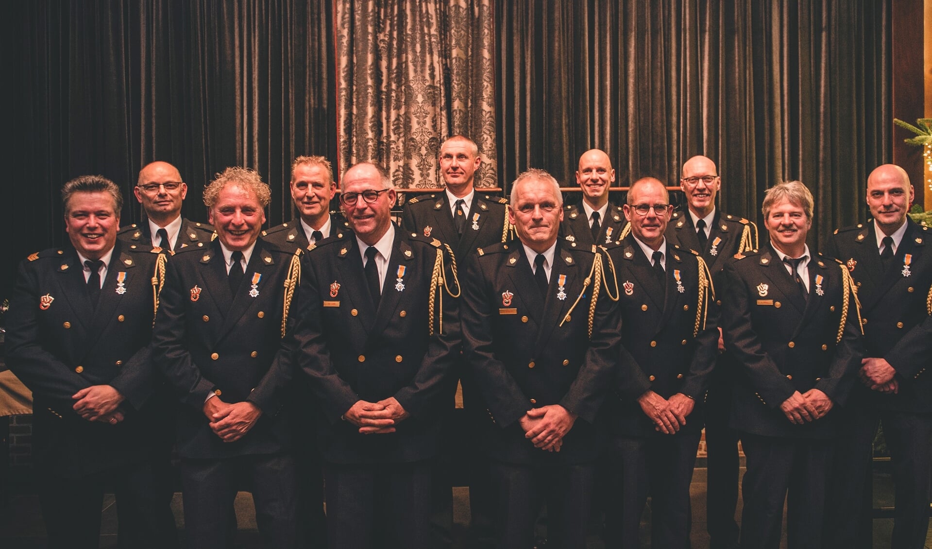 Maar liefst twaalf brandweervrijwilligers van de post Ruurlo ontvingen de Koninklijke Onderscheiding Lid in de Orde van Oranje-Nassau uit handen van burgemeester Joost van Oostrum (r). Foto: Matthijs Weenk