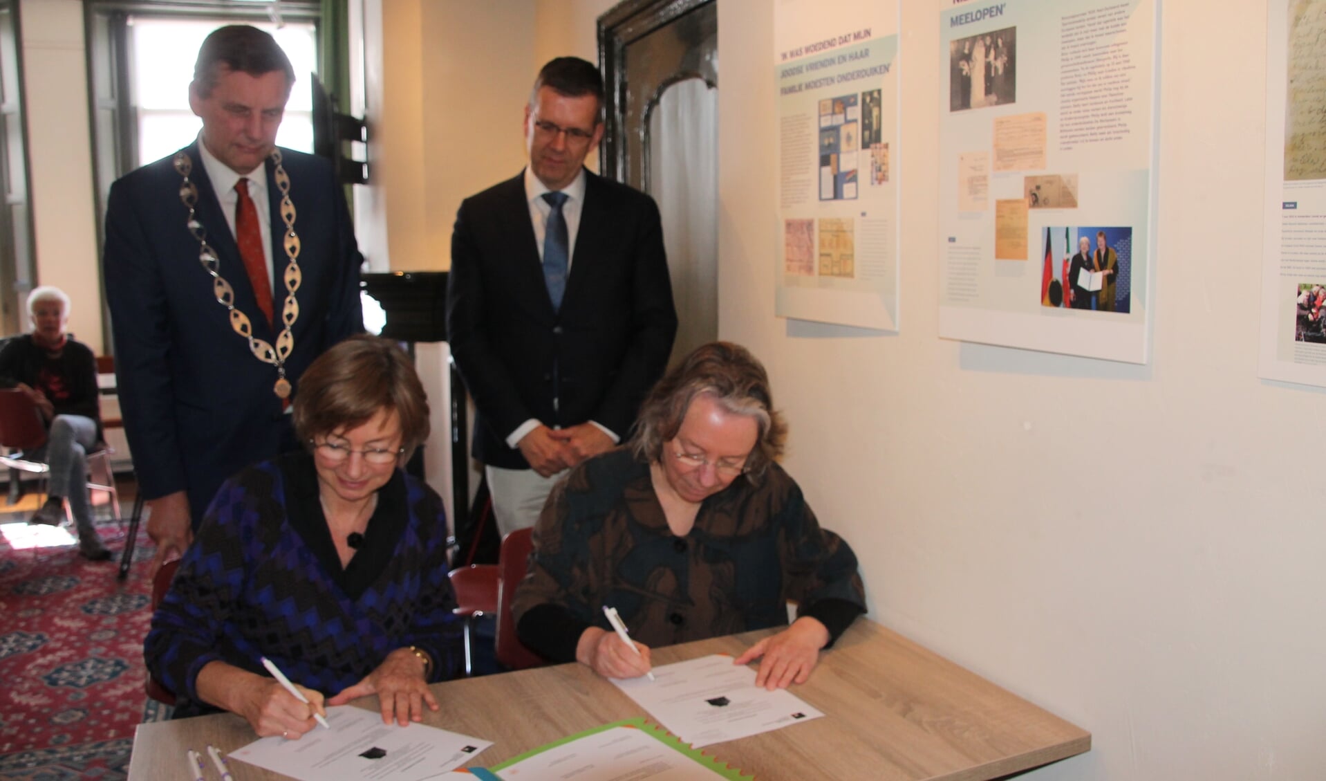 De ondertekening van de overdracht door Gerda Brethouwer en Claire Vaessen (rechts). Burgemeester Anton Stapelkamp en loco-burgemeester Joost Reus (staand rechts) kijken toe. Foto: Lydia ter Welle