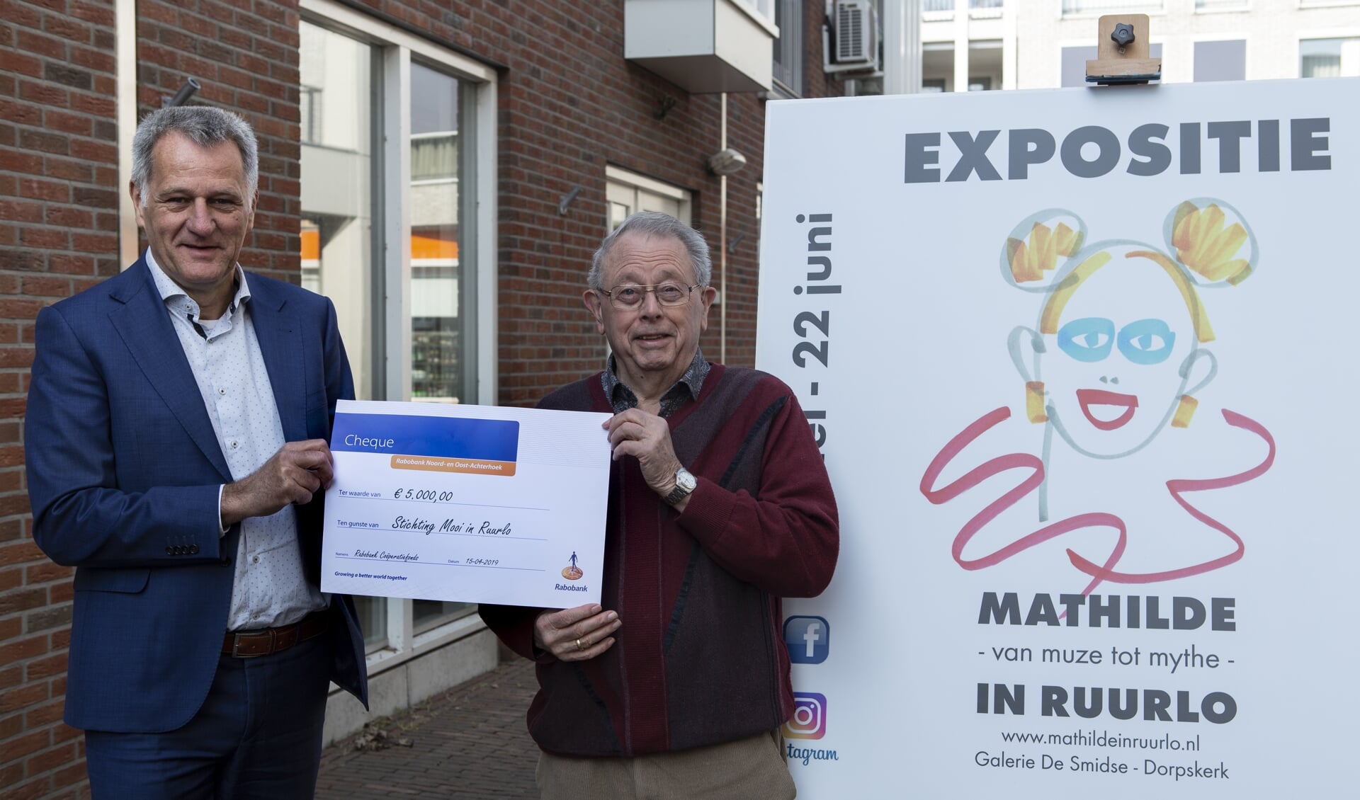 Laurens Stapelbroek van Rabobank Noord- en Oost-Achterhoek overhandigt een cheque ter waarde van vijfduizend euro aan Joop Huisman voor de deur van galerie De Smidse. Foto: PR