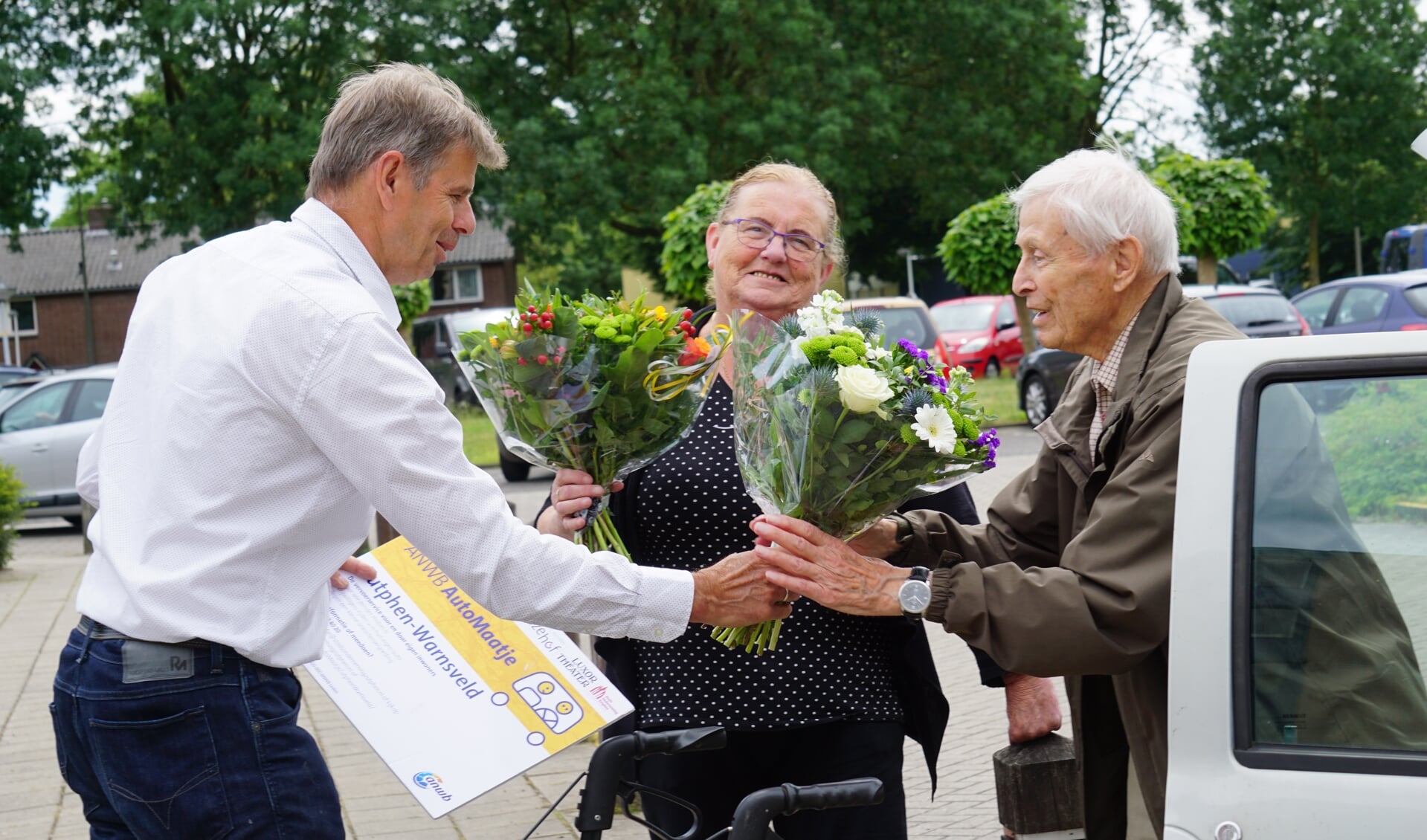 Chauffeur Joke van Campen en de 91-jarige Diewulf Baatz worden na de 1500ste rit door Lex Hemelaar van burgerinitiatief Stadsonderneming Zutphen in de bloemetjes gezet. Foto: PR
