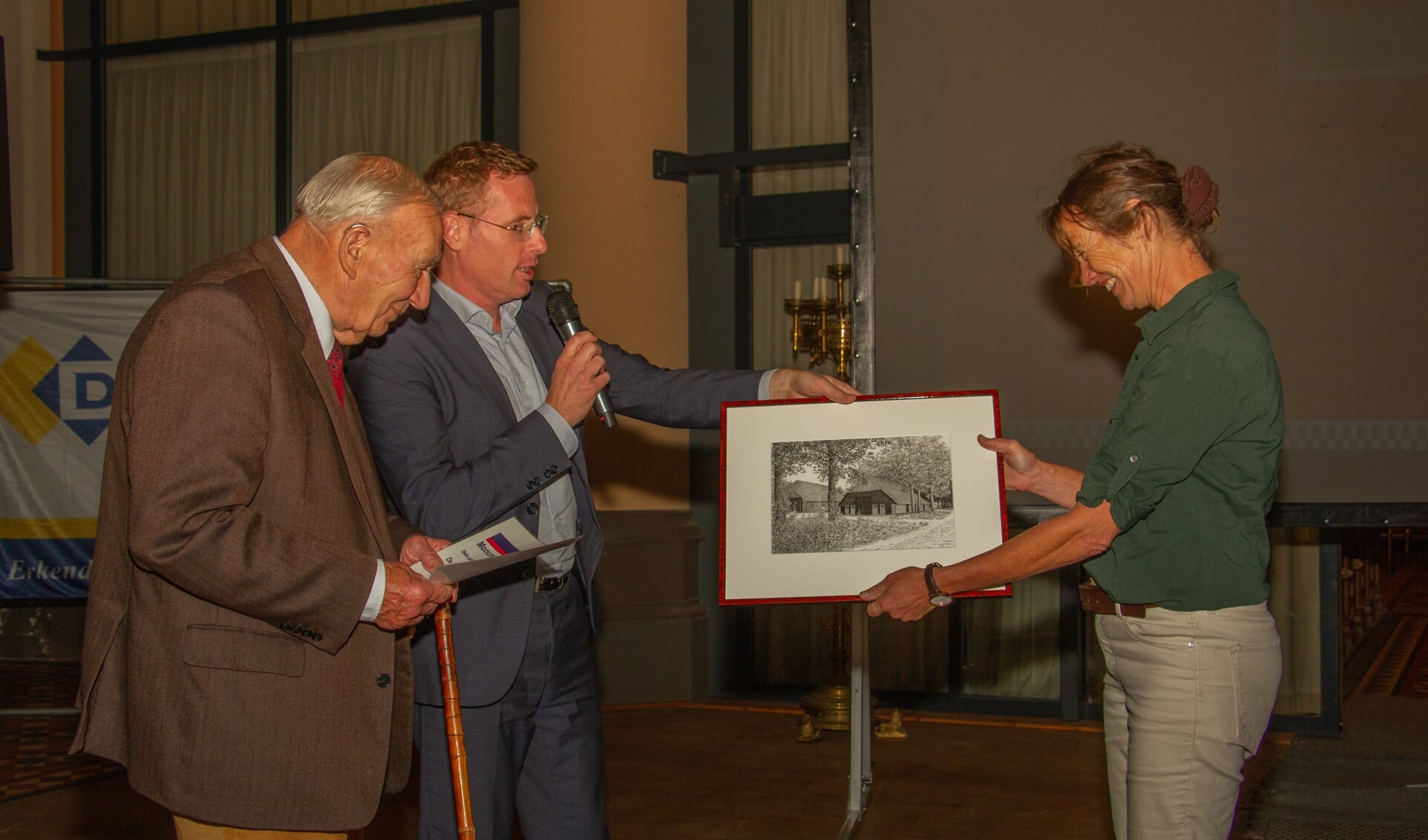 Wethouder Willem Buunk overhandigt de cheque aan Jan Markvoort en de pentekening van de eekschuur aan dochter Elisabeth. Foto: Liesbeth Spaansen