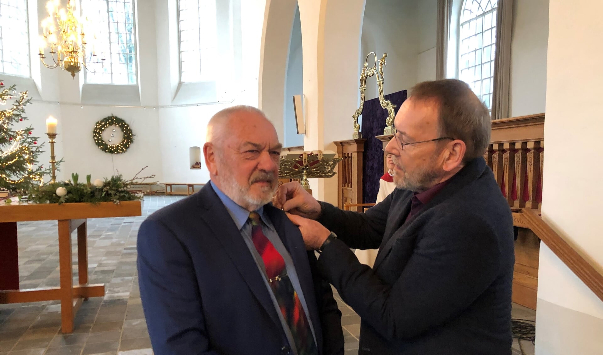 Riek Linde krijgt het draaginsigne in zilver van de Protestantse Kerk opgespeld door kerkrentmeester Luc van Asselt. Foto: PR