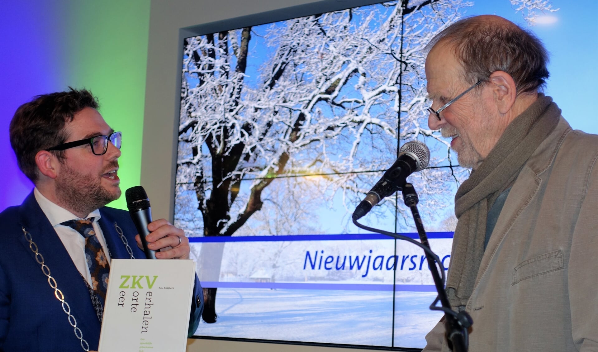 Burgemeester Sebastiaan van 't Erve overhandigt het eerste exemplaar van de gebundelde ZKV's, die A.L. Snijders (r) voordroeg tijdens eerdere nieuwjaarsrecepties van de gemeente uit aan  de schrijver. Foto: Henri Bruntink