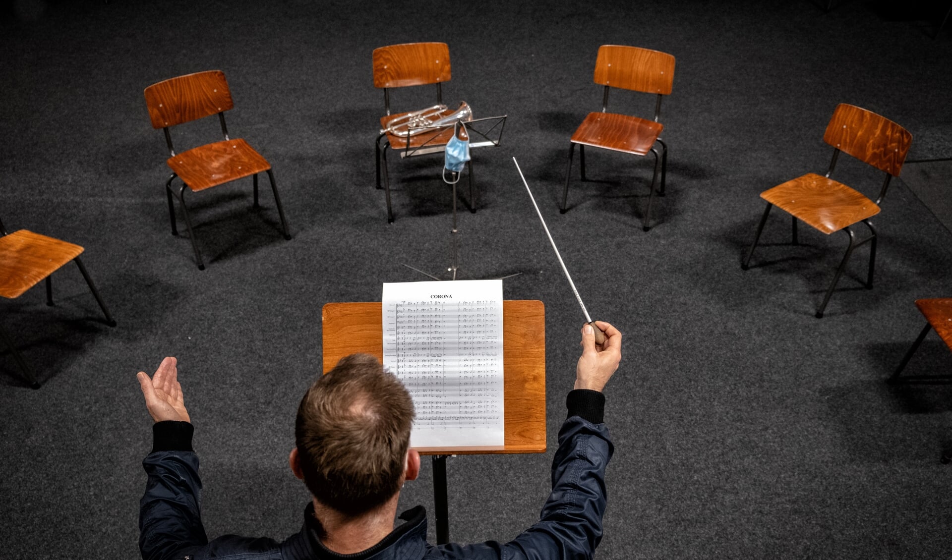 Dirigent Egbert van Groningen symboliseert in een leeg clubgebouw, een paar lege stoelen en een verlaten instrument de stille periode die het orkest meemaakt. Foto: Mathijs Roelofsen