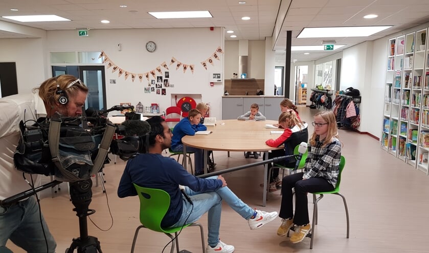 Cameraman Bjarne, verslaggever Ruwan en de kinderen Britt, Anniek, Naomi, Trysten, Menno en Dylan tijdens de opnames van het Jeugdjournaal met rechts de bibliotheek. Foto: Han van de Laar