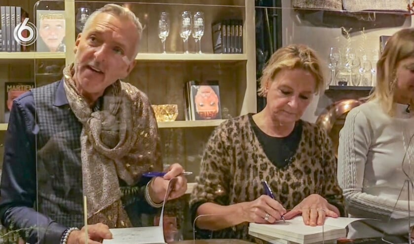 <p>Martien Meiland en Erica Renkema signeren achter een spatscherm de biografie van Martien. Foto: PR</p>