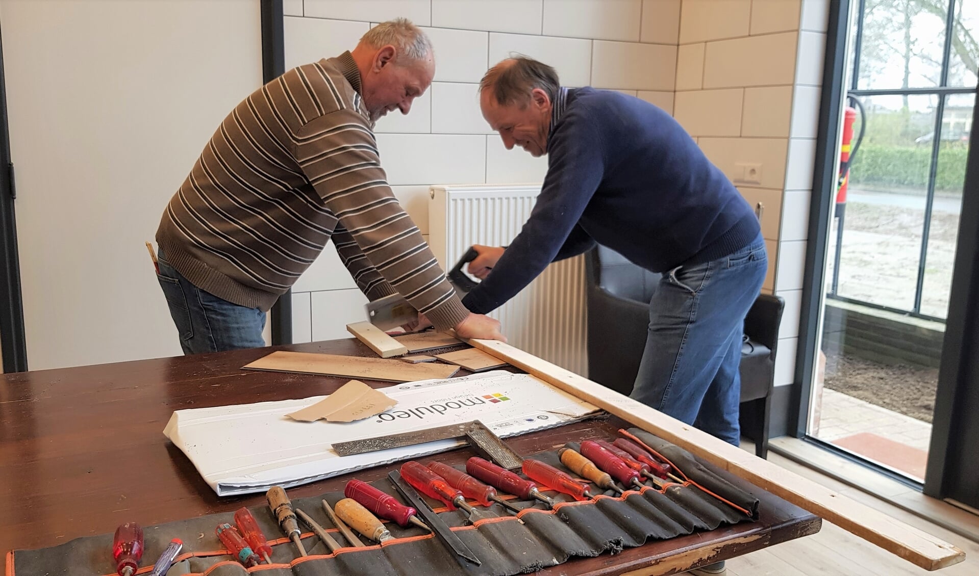 Guus Willemsen (l) en Cor Slakhorst, twee van de grote groep vrijwilligers van de bouwploeg van De Kei, zagen een plank op maat voor een vloertje in een muurkast. Foto: Alice Rouwhorst