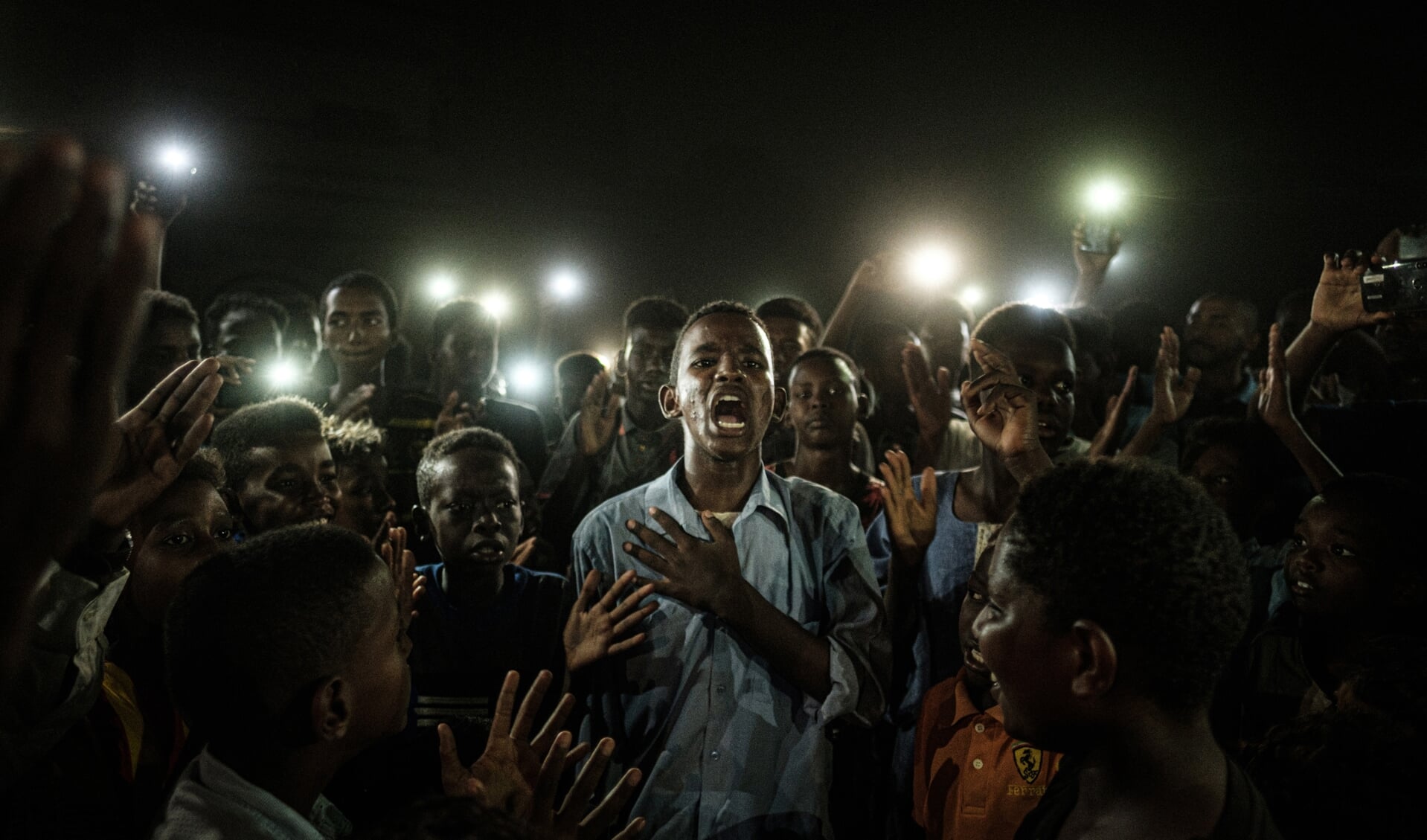Overall winnaar is de foto Straight Voices van de Japanse fotograaf Yasuyoshi Chiba. Deze foto is gemaakt tijdens een black-out in Soedan, in juni 2019. Een jonge Soedanees die protestgedichten voordraagt, wordt verlicht door mobiele telefoons. De demonstranten om hem heen roepen op tot een burgerregering. De fotograaf zei over zijn beeld: “Dit was het enige vreedzame groepsprotest dat ik tijdens mijn verblijf tegenkwam. Hun onverslagen solidariteit voelde als brandende sintels die nog moeten oplaaien.” Foto: Yasuyoshi Chiba/AFP 