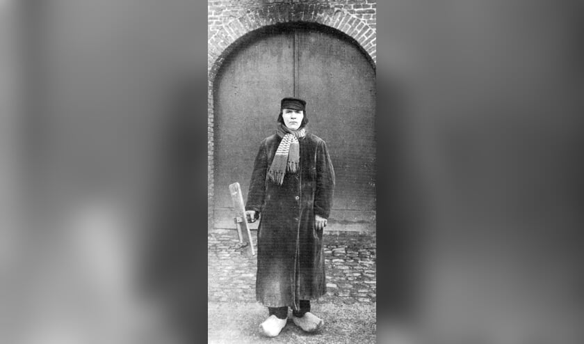 G. Bretveld in wintertenue voor de torendeur van de NH-kerk: duffelse pet met oorkleppen en stormband, das, ulster en klompen. In zijn rechterhand de klepper. Foto archief W. Hermans