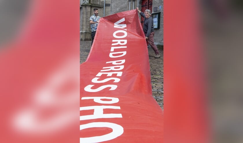 De banner ligt uitnodigend als een rode loper voordat hij aan de gevel van de Walburgiskerk wordt bevestigd. “World Press Photo is voor de zesde keer in Zutphen. Normaal gesproken is de tentoonstelling wereldwijd in negentig steden te zien. Nu slechts in negen steden, waarvan Zutphen er één van is. We hebben geluk dat de Walburgiskerk de ruimte biedt.” Links Patrick van Gemert en rechts Arjen Woudenberg, inspirators en organisatoren van het eerste uur. Foto: Gerard Mühlradt