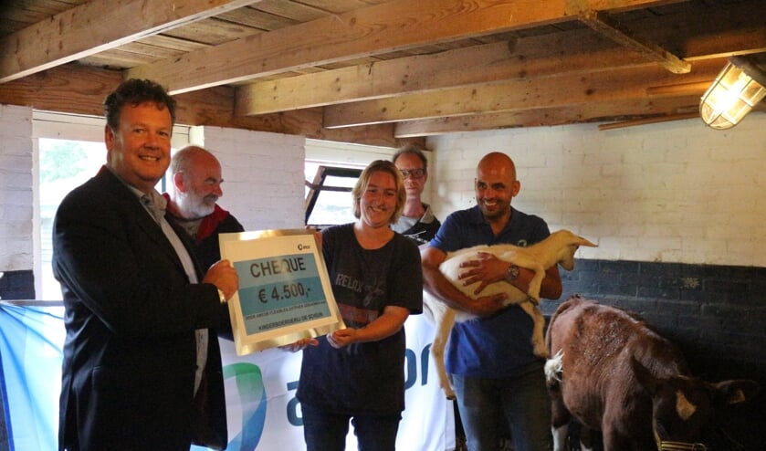 Erwin van Tienoven van Amcor overhandigt de cheque aan Cynthia Imhoff (vervangend beheerster van de Schouw). Een medewerker van Amcor, Massimo Scanu, houdt de geit vast. De heren achteraan zijn cliënten van Zozijn, samenwerkingspartner van de kinderboerderij. Foto: PR