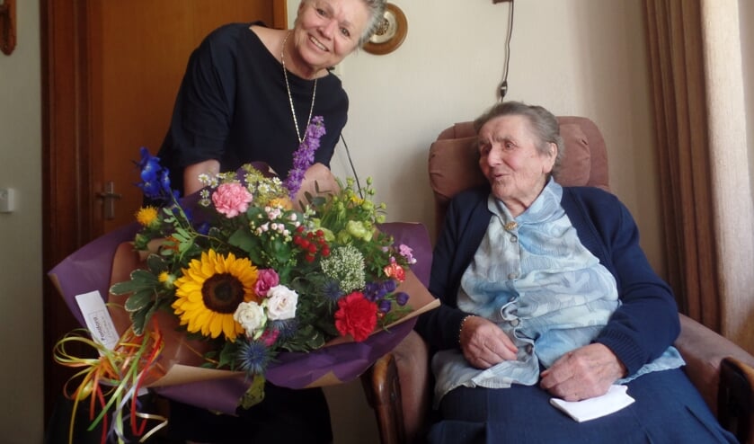 Verrast kijkt Dientje Neerlaar naar het prachtige boeket dat wethouder Marijke van Haaren aan de honderdjarige schenkt. Foto: Jan Hendriksen.