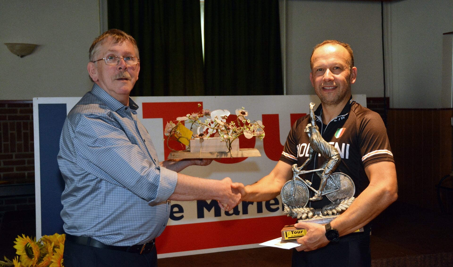  In 2019 won Derk ter Horst uit Bredevoort de 36e Tour de Mariënvelde. Hij krijgt hier uit handen van Henny Heutinck (links) de trofee overhandigd.
Foto: PR