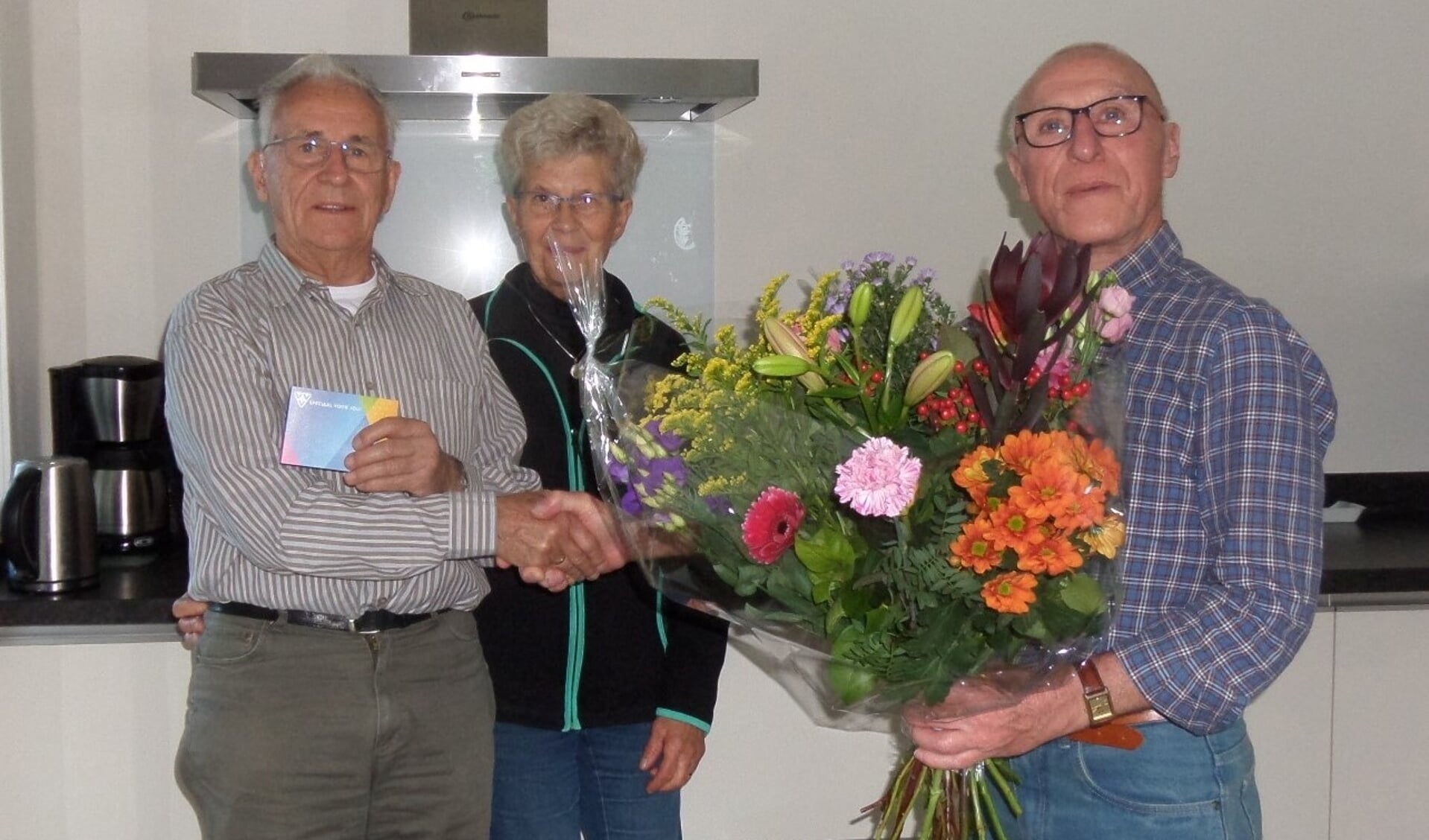Uit handen van voorzitter Bertus Nijenhuis van EHBO Vorden (r.) ontving jubilaris Martin Wolsing een cadeaubon. Voor zijn vrouw Diny was er een mooie bos bloemen. Foto: PR