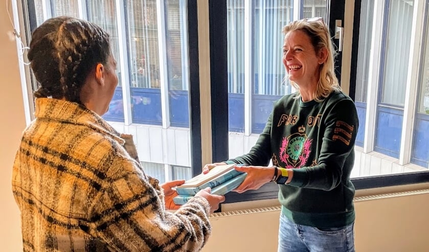 <p>Hellen Strik overhandigt in Het Stadshuus kinderboeken aan een ouder. Foto: Henri Bruntink</p>