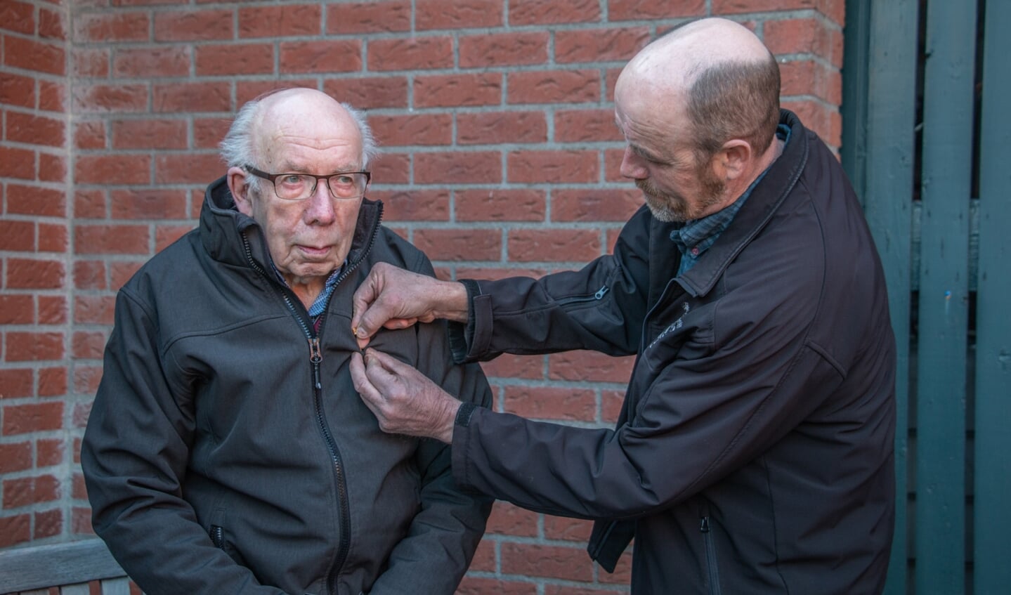 Gerrit Teunissen krijgt via zoon Lammert een speld op zijn jas voor zijn 70-jarig lidmaatschap van muziekvereniging Hummelo en Keppel. Foto: Liesbeth Spaansen