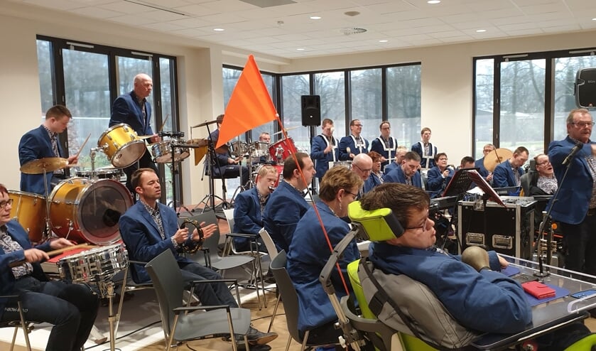 <p>Tonnie Weikamp staand te midden van muzikanten van de Rainbowband tijdens een optreden bij Zozijn in Wilp. Foto: eigen foto.</p>