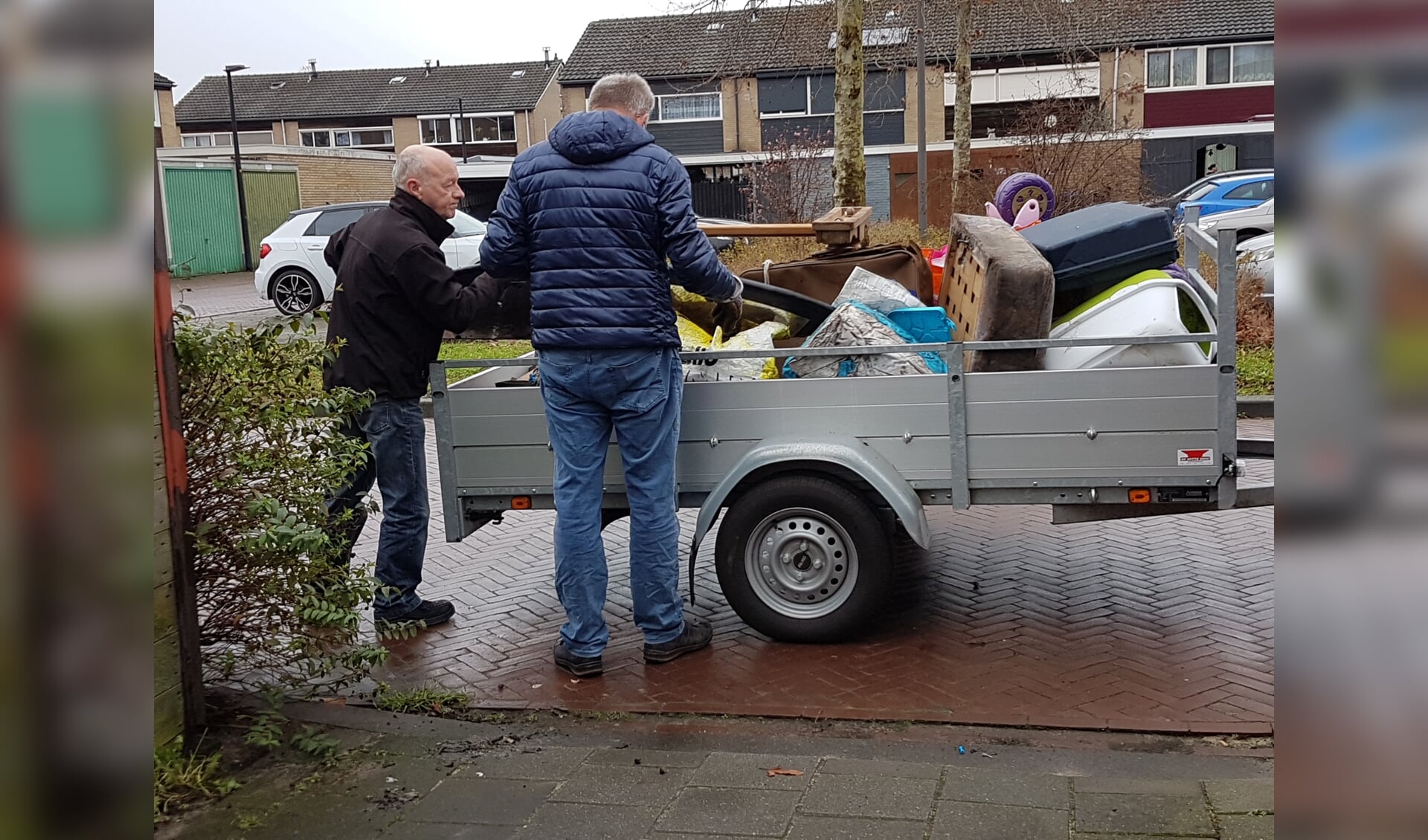 Twee vrijwilligers laden een aanhangwagen vol tijdens een opruimklus. Foto: Present Winterswijk