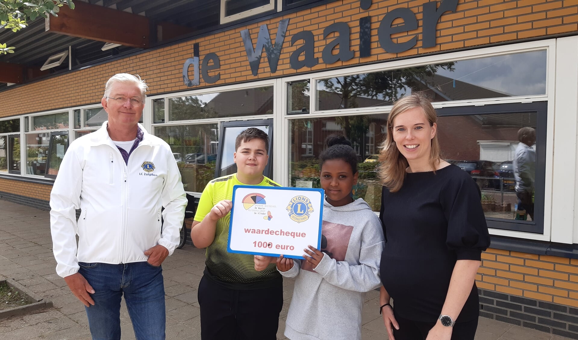Willem Ringenier van de Lionsclub Zutphen (l) overhandigt de cheque aan leerlingen Collin Tazelaar en Delina Heshelu in het bijzijn van leerkracht en taalcoördinator Esmée Vakkert (r). Foto: PR