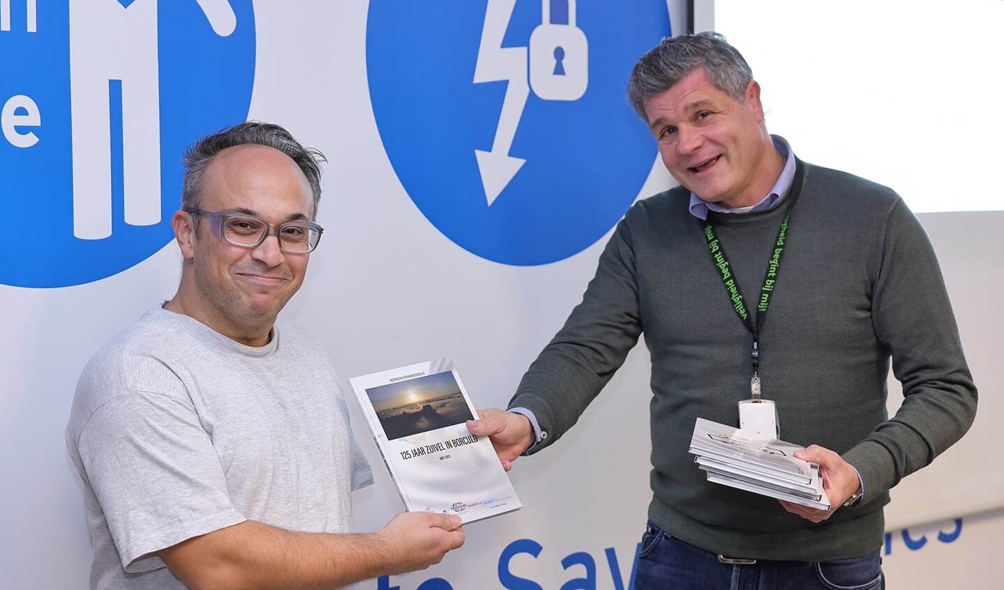 Werknemer Ilker Kavakli ontvangt het jubileumboekje uit handen van plant manager Eric Hassink (r). Foto: PR/De Vrolijke Foto