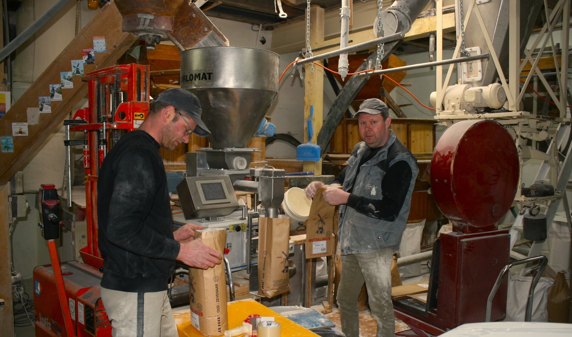 Simon Goossens en George Pijnappel vullen zakken meel in de maalderij van molen De Vier Winden. Foto: Jos Betting