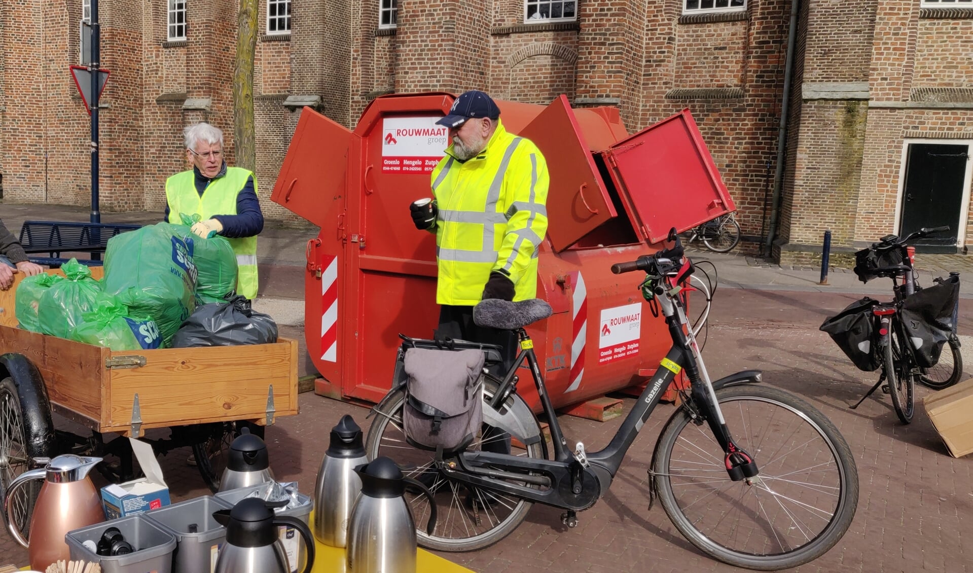 Sjef Taken, Harry Bosch en Berend Meerbeek (v.l.n.r.) met het nodige zwerfvuil bij de rode verzamelcontainer op het Ruurlose Kerkplein.  Foto: PR.