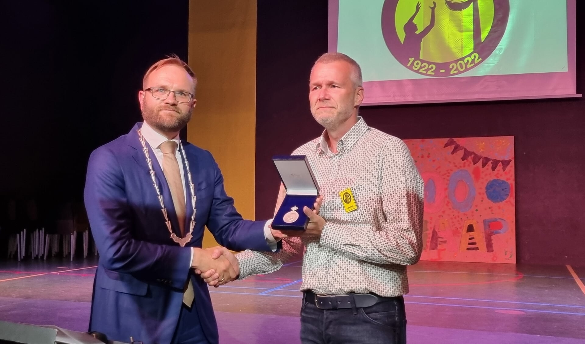 Wethouder Teselink reikt de Koninklijke Erepenning uit aan korfbalvoorzitter Erik Huijsmans ter gelegenheid van honderd jaar Olympia ’22. Foto: Rob Weeber