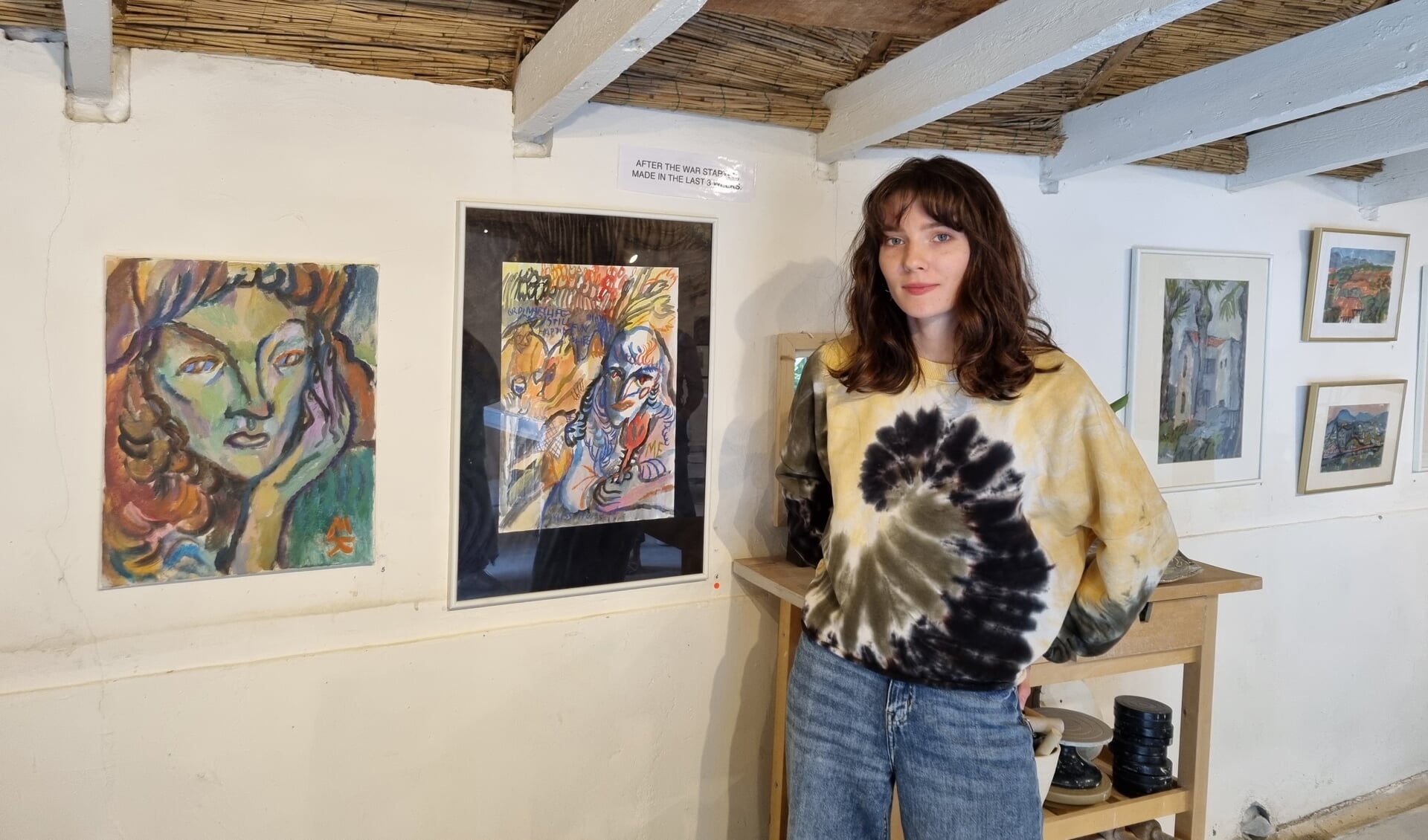 Kunstenares Maria Kitaeva; links van haar de schilderijen voor de inval van de Russen en rechts haar zelfportretten na de inval. (Foto: Rob Weeber