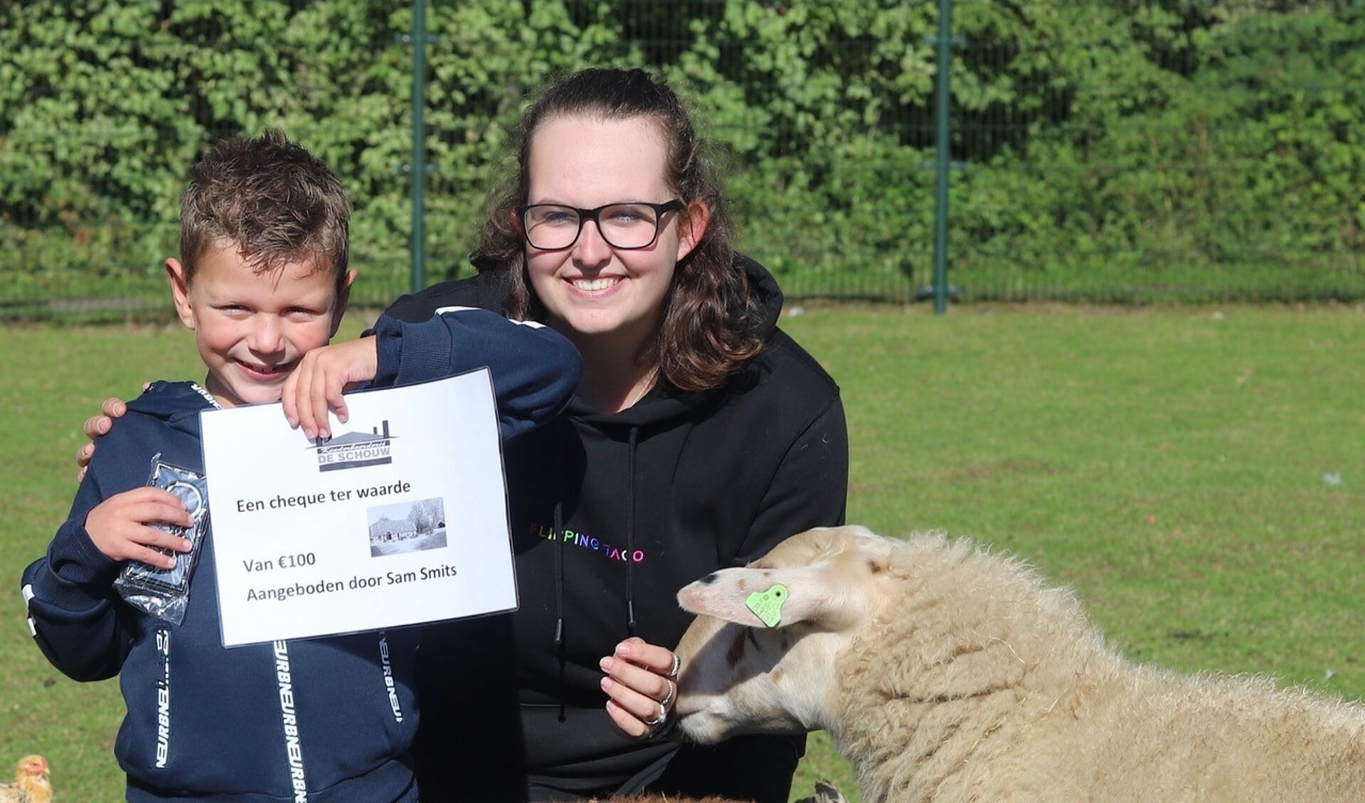 Sam Smits met cheque en sleutelhangers en beheerder Anne Derksen tussen de schapen op kinderboerderij De Schouw. Foto: Sander Grootendorst