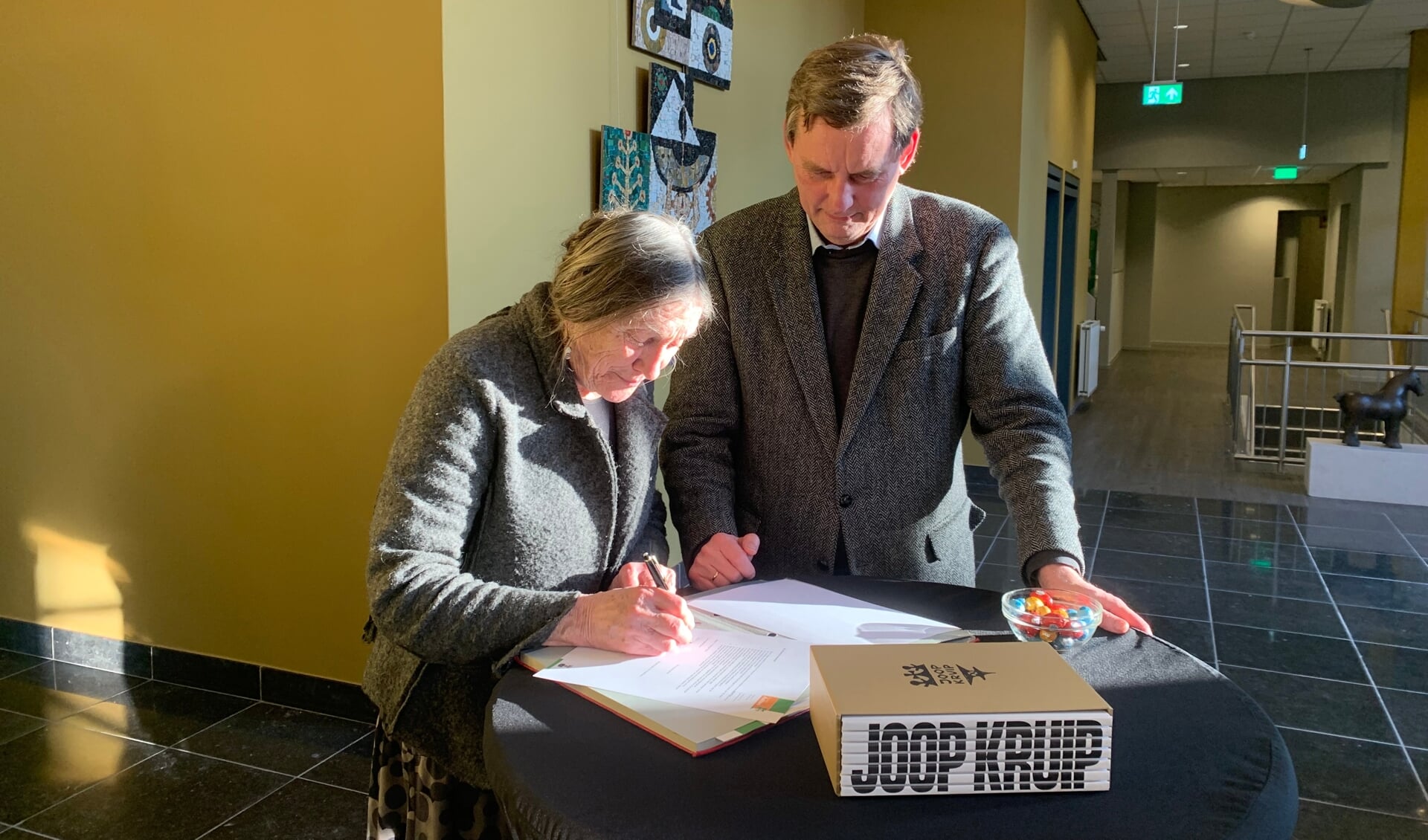 Burgemeester Anton Stapelkamp en Minnie Kruip tekenen de bruikleenovereenkomst. Op de voorgrond het foedraal met de zeven boeken Joop Kruip. Foto: Jos Wessels