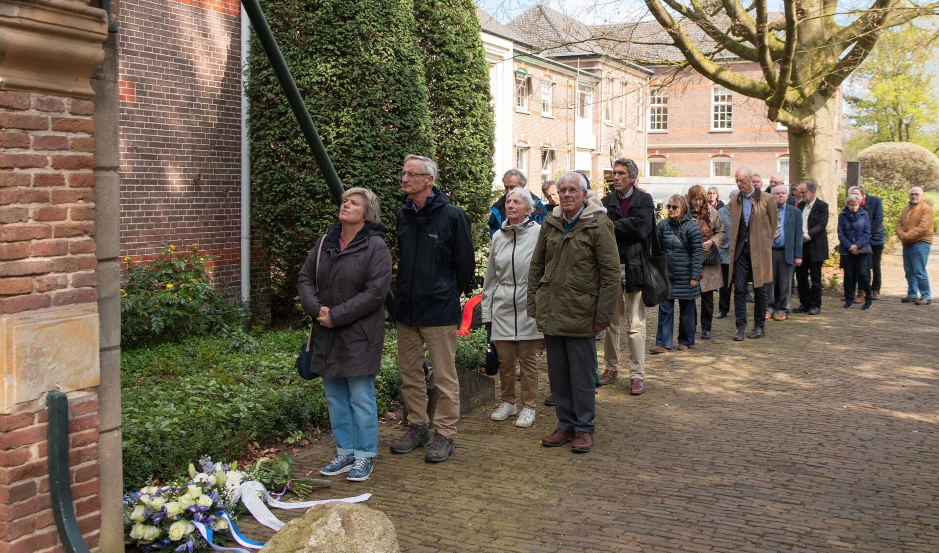 Bezoekers lopen langs de plaquette, waaronder bloemen zijn neergelegd. Foto: Henk Derksen
