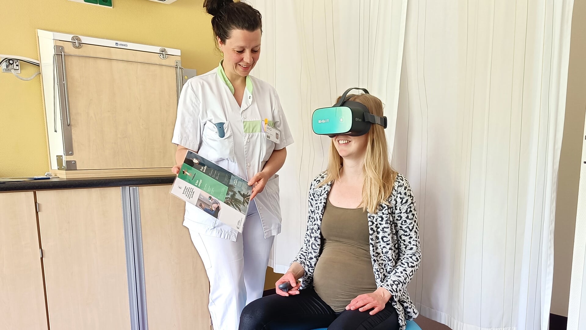 Obstetrieverpleegkundige Lotte Kroeze-Roolvink helpt een zwangere patiënt bij het gebruik van de VR-bril. Foto: PR SKB