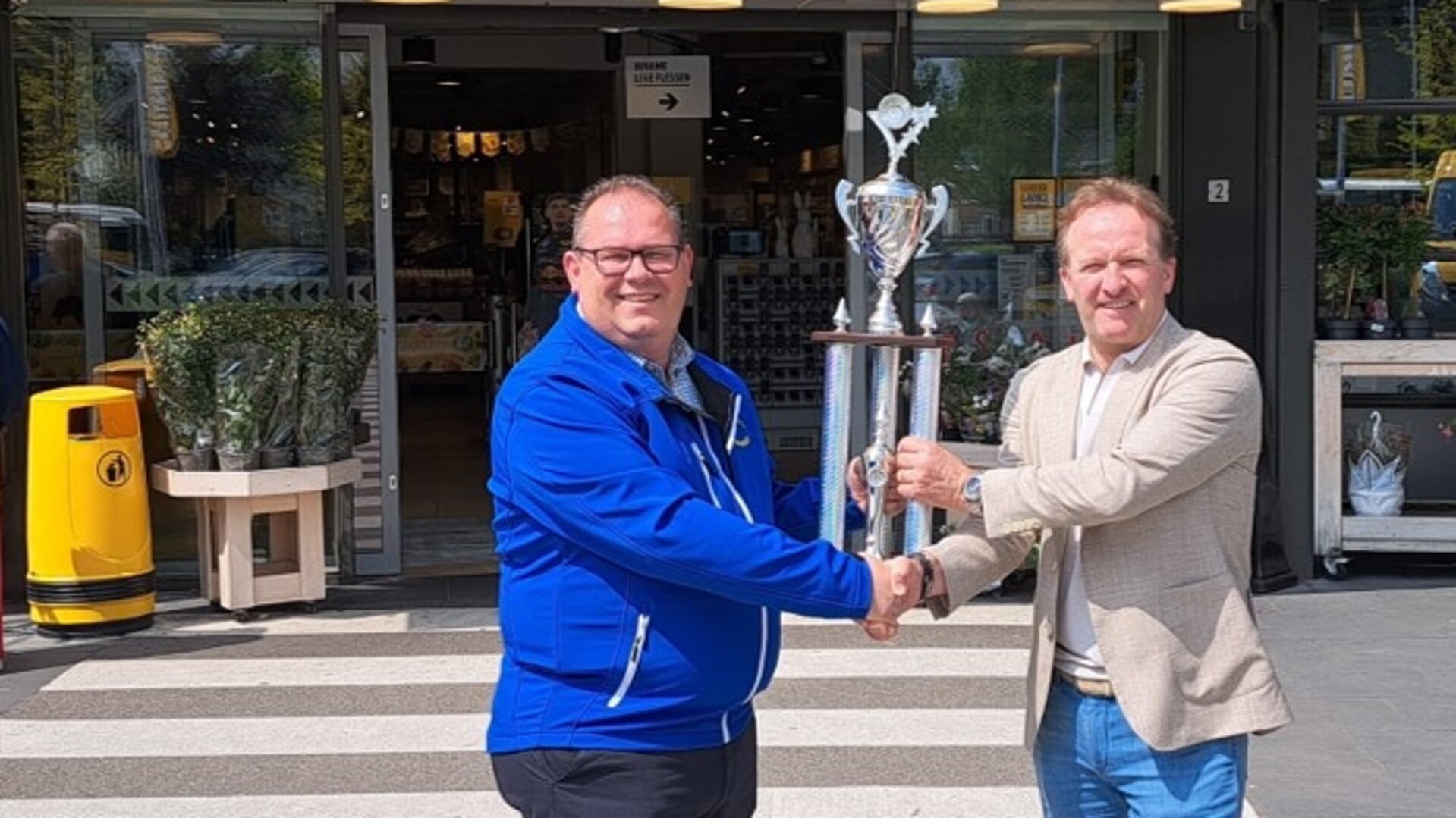 Voorzitter van het Open Achterhoeks Dweilorkesten Kampioenschap Frank Beurskens (links) neemt de nieuwe hoofdprijs in de Leutklasse in ontvangst uit handen van Pascal Bennink. Foto: PR