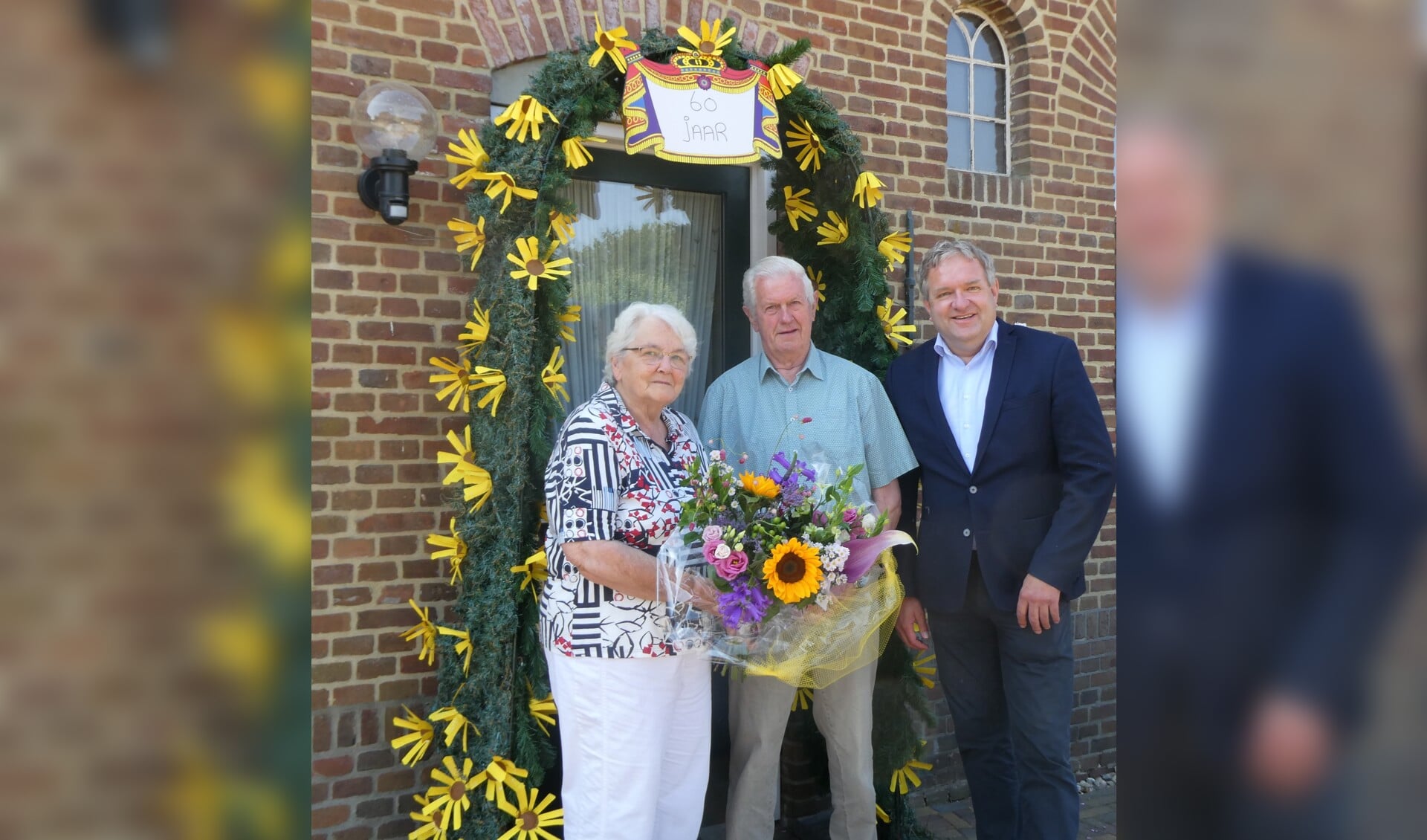 Aaltje en Arend Megelink samen met locoburgemeester Arjen van Gijssel bij de boog die met 'zonnebloemen' was versiert. Foto: Jan Hendriksen, 