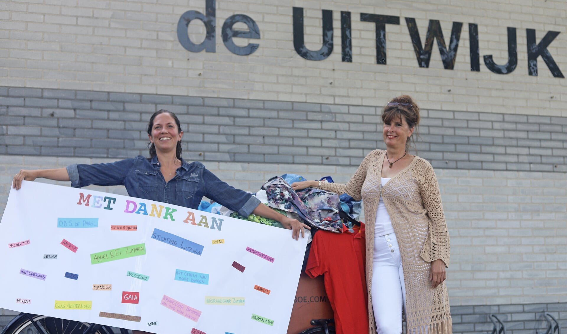Jolyne Klein Paste (links) en Greet Zweers bij de kleding-ophaalbakfiets voor het buurthuis. Op het grote vel papier de namen van iedereen die het initiatief een warm hart toedraagt.
