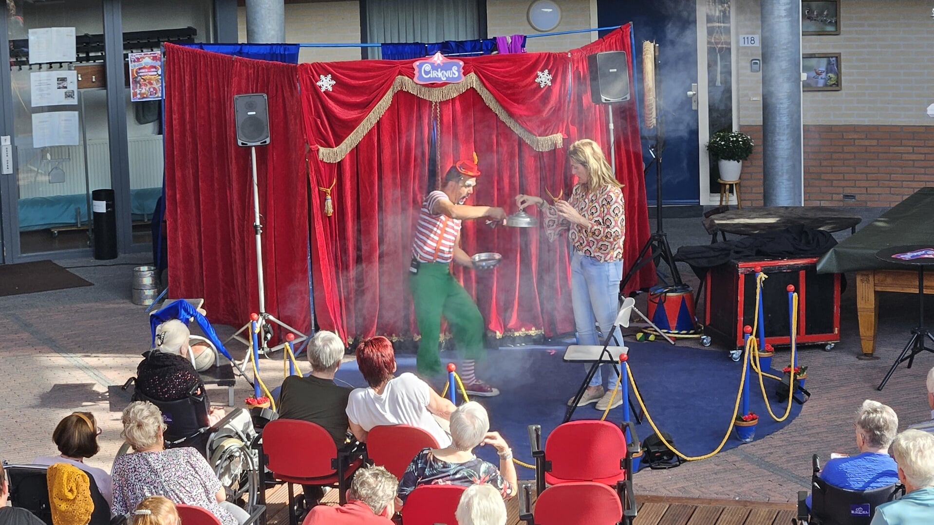 Bewoners van De Molenberg genieten van een circusvoorstelling van Cirknus in d' Orangie. Initiatiefneemster Christa Heijstek assisteert de clown. Foto: Dinès Quist