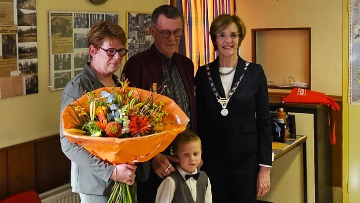 Erelid Marcel van Melis kreeg een lintje opgespeld door burgemeester Bronsvoort. Monique van Melis en kleinzoon Melis poseren mee.