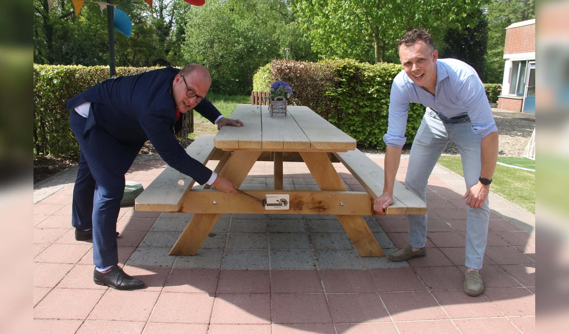 Burgemeester Joris Bengevoord (l) en Constantijn Schreiber bevestigen samen het naamplaatje van houthandel Nijweide op de picknicktafel. Foto: Lineke Voltman