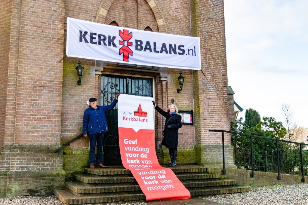 Joke Cornelissen en Jan van Dijk hangen de vlaggen uit om iedereen te wijzen op de actie Kerkbalans. Foto: Wietse van den Berg