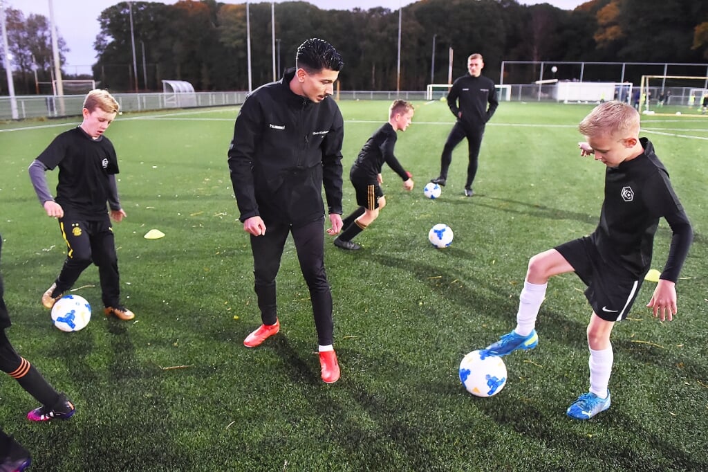 Kaan Ozerdogan leert de voetballers een bepaalde techniekvorm. Matthijs van Nispen kijkt op de achtergrond mee. Foto: Roel Kleinpenning
