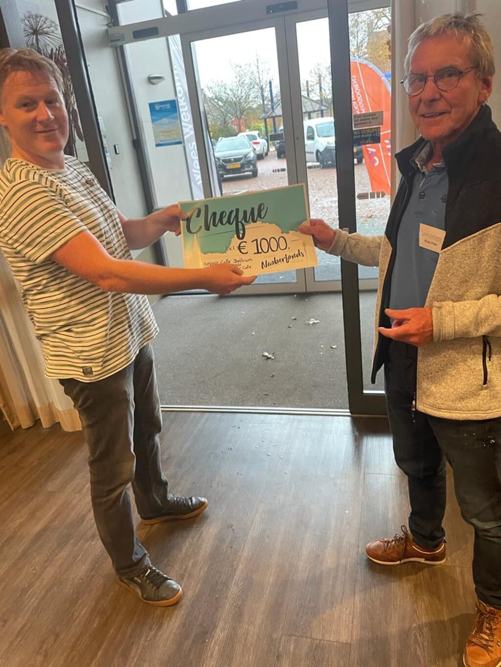 Een cheque van duizend euro voor het Repair Café vanuit het Noaberfonds, uitgereikt door Bart Ribbers aan initiatiefnemer Aloys Pape. Foto: PR